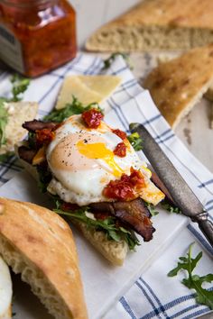 an open face sandwich with bacon, eggs and cheese on it next to bread slices