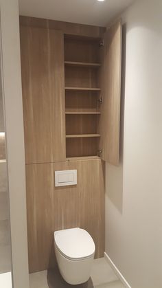 a white toilet sitting inside of a bathroom next to a wooden shelf filled with books