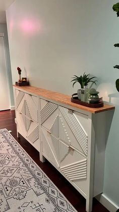 a white sideboard with two plants on top and a rug in the corner next to it