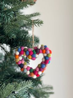 a heart shaped ornament hanging from a christmas tree with pom - poms