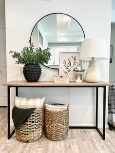 a table with two baskets and a round mirror on the wall above it, next to a lamp