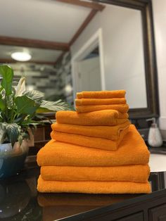 a stack of orange towels sitting on top of a counter next to a potted plant