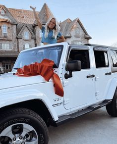 a woman standing on top of a white jeep with an orange ribbon tied around it