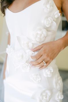 a woman wearing a wedding dress with flowers on the side and her hand in her pocket