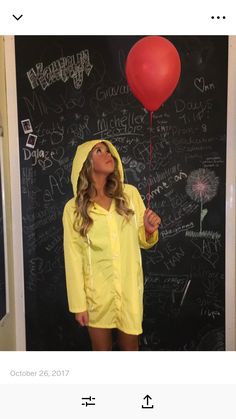 a woman wearing a yellow raincoat and holding a red balloon in front of a blackboard