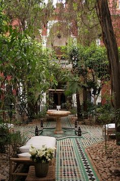 an outdoor courtyard with potted plants and tables in the center, surrounded by greenery