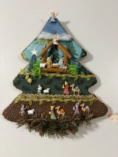 an ornament is hanging on the wall in front of a christmas tree with nativity