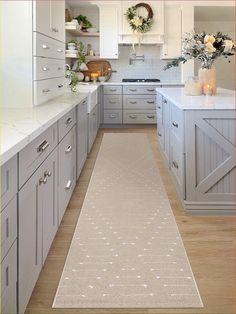 a long narrow kitchen with white cabinets and light wood flooring, along with an area rug in the middle