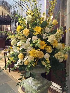 a vase filled with yellow and white flowers sitting on top of a stone pedestal in front of a window