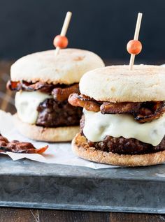 two hamburgers with meat and cheese on them sitting on top of wax paper next to toothpicks