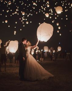 a bride and groom are holding lanterns in the air as they fly through the night sky