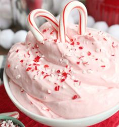 a bowl filled with pink frosting and two candy canes on top of it