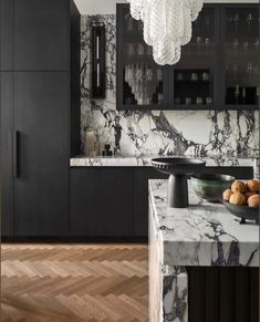 a kitchen with marble counter tops and black cabinetry, along with a bowl of fruit