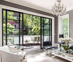 a living room filled with furniture and a chandelier hanging from the ceiling over a glass top coffee table