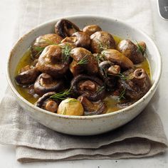 a white bowl filled with mushrooms on top of a table next to a fork and napkin