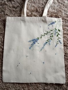 a white bag with blue flowers painted on it sitting on the floor next to a pair of scissors