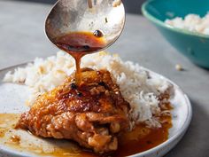 someone is pouring sauce on some food on a plate with white rice and blue bowl in the background