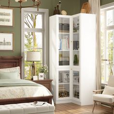 a bedroom with a bed, chair and bookshelf next to two windows in the room