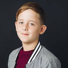 a young boy wearing a gray jacket and red shirt posing for a photo in front of a black background