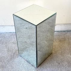 a mirrored cube table sitting on the floor in front of a white wall and carpet