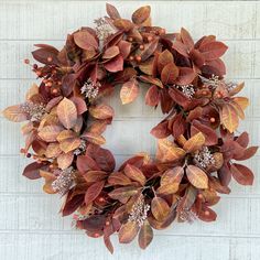 a wreath with red and green leaves hanging on a white brick wall in front of a door