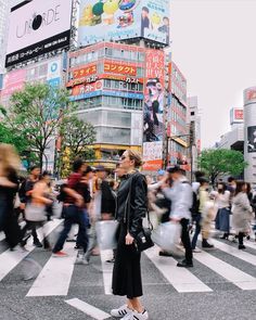 a woman standing in the middle of a crosswalk with lots of people walking around