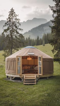 a yurt in the middle of a grassy field with mountains in the back ground