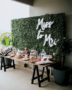 a table topped with lots of desserts next to a wall covered in greenery