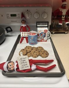 an elf is sitting on top of the stove with cookies and hot cocoa in front of him