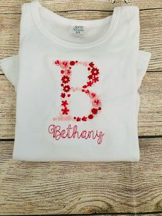 Beautifully embroidered single letter monogram with pink and red threads to create this sweet design. This floral font is available in all letters of the alphabet. A monogram name below the design is included with the font of choice. Ballerina font is shown in the sample. Shirt is a 100% cotton long sleeve white shirt with ruffle hem. Other shirt colors and sleeve sizes may be available, please message us to check inventory. Single Letter Monogram, Long Sleeve White Shirt, Flower Girl Shirts, Floral Font, Alphabet A, Letter Monogram, Flower Letters, Single Letter, White Long Sleeve Shirt