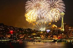 fireworks are lit up in the night sky over water and city buildings with lights on them