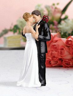 a bride and groom figurine standing next to each other in front of flowers