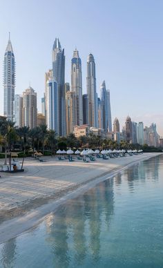 an empty beach with umbrellas and chairs in front of the city's skyscrapers