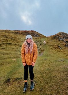 a woman standing on top of a grass covered hillside next to sheep in the distance