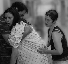 a pregnant woman wrapped in a blanket is being hugged by two men as they stand next to each other