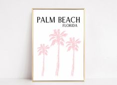 a pink palm tree print hangs on a white wall in front of a gold frame