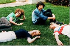 four young people laying on the grass in front of a house and one person standing