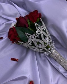 a brides bouquet with red roses and diamond tiara sits on a purple satin