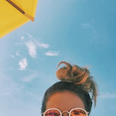 a woman with sunglasses on her head is looking up at the sky and there are yellow umbrellas in the background