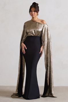 a woman in a black and gold gown with an open cape over her shoulders, posing for the camera