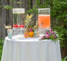 two glass jars filled with fruit sitting on top of a white table covered in greenery