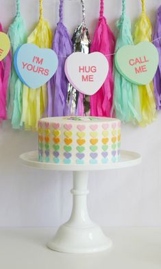 a cake sitting on top of a white cake plate next to tassels that say hug me and i'm yours