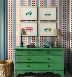 a green dresser sitting next to a wall with pictures above it and two lamps on top