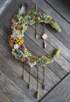 a wreath made out of moss and flowers on a wooden floor with two spoons hanging from it