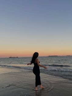 a woman standing on top of a sandy beach next to the ocean at sunset or dawn