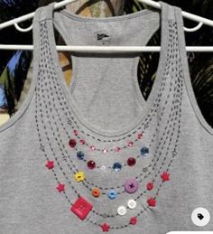 a gray tank top with multi colored buttons and chains hanging on a clothes rack in front of palm trees