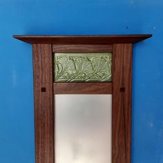 a wooden mirror hanging on the wall next to a blue wall with a green leaf design