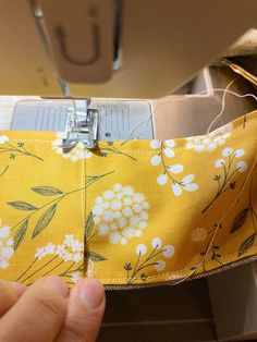 someone is stitching the lining on a yellow fabric with white flowers and green leaves