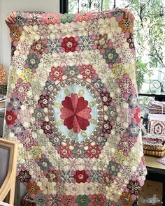 a woman holding up a large quilt in front of a window with flowers on it