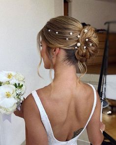 a woman in a white dress holding a bouquet of flowers and looking at the mirror